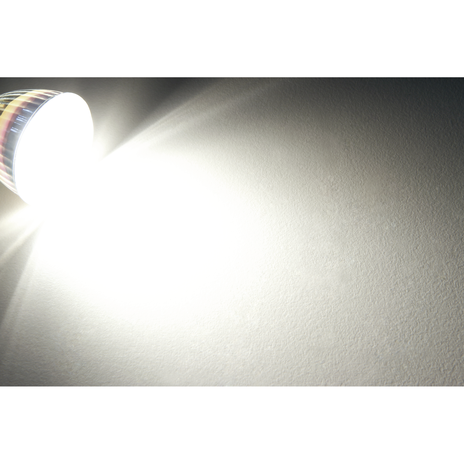 Ein helles Licht scheint auf eine weiße Wand. Der Hintergrund ist schwarz.