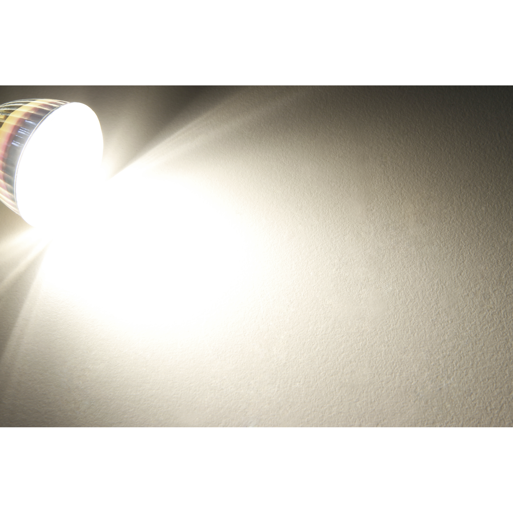 Helles Licht einer Glühbirne scheint auf eine strukturierte, cremeweiße Wand und erzeugt einen hellen Bereich.