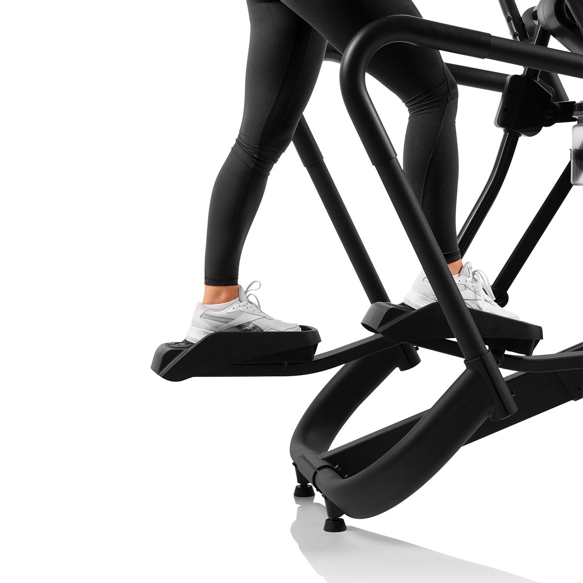 Person benutzt ein Ellipsentrainer, Beine sichtbar, trägt weiße Turnschuhe und schwarze Leggings.