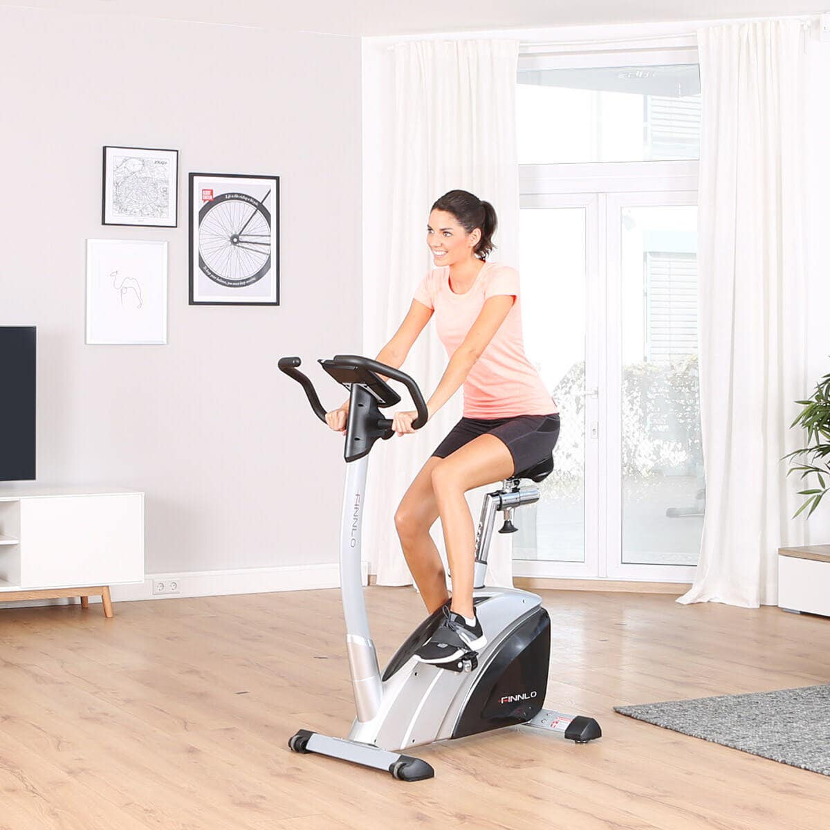 Eine Frau trainiert auf einem Heimtrainer in einem hellen Raum mit Kunst an der Wand.