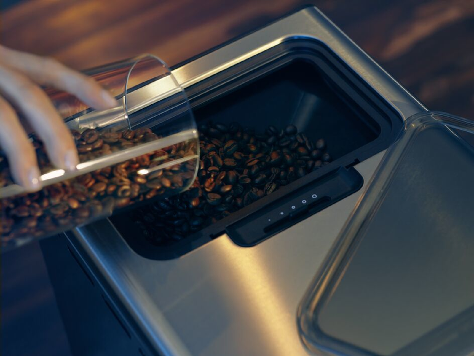 Eine Person gießt Kaffeebohnen in einen Behälter. Holztisch mit der Kaffeemaschine. Nahaufnahme.