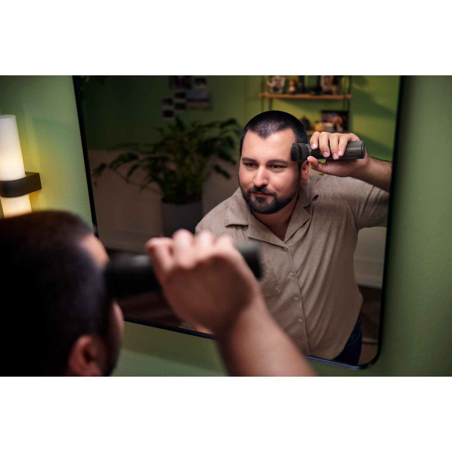 Hombre mirándose en un espejo, recortando su cabello con un recortador eléctrico.
