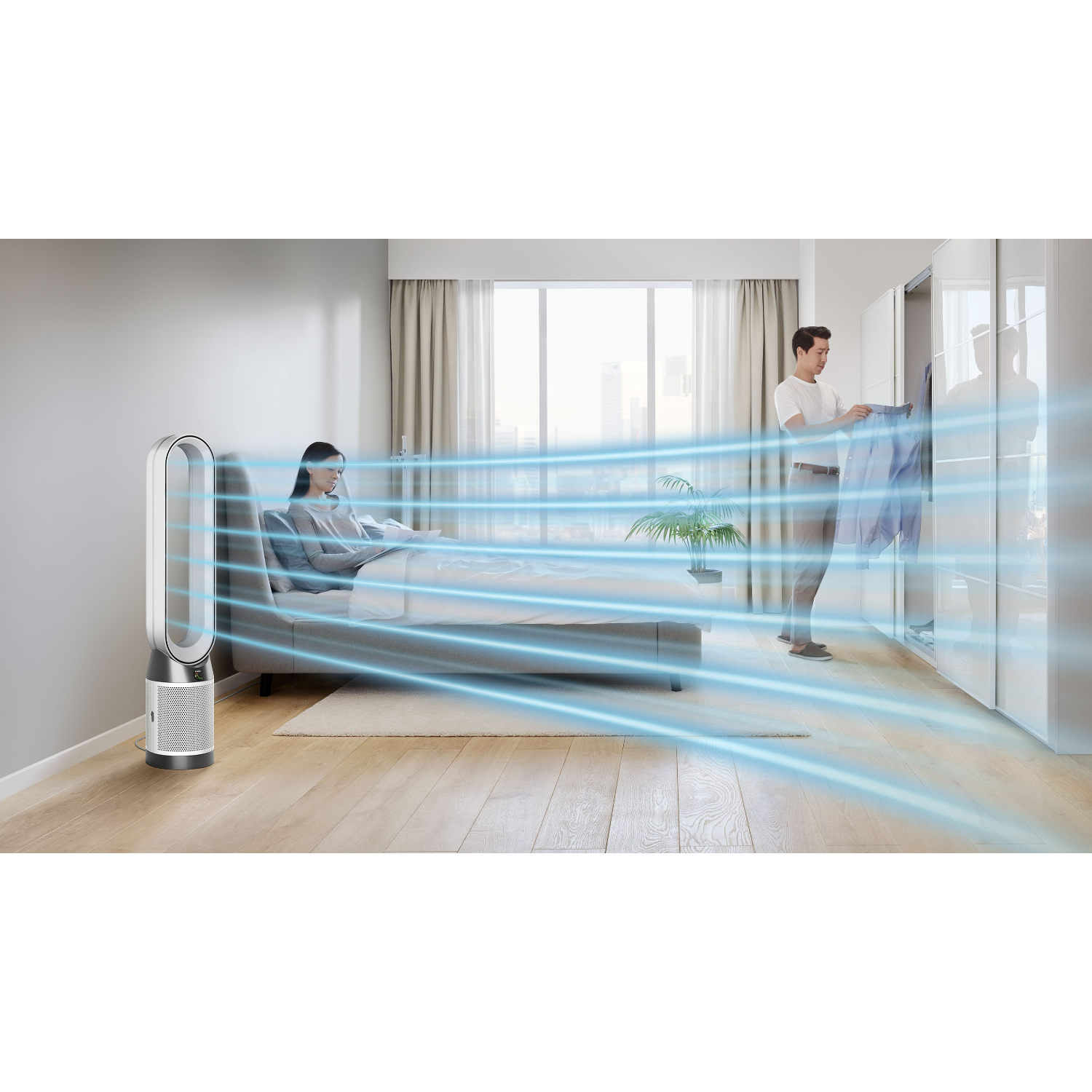 Una mujer sentada en una cama con un purificador de aire, y un hombre cerca de un armario.