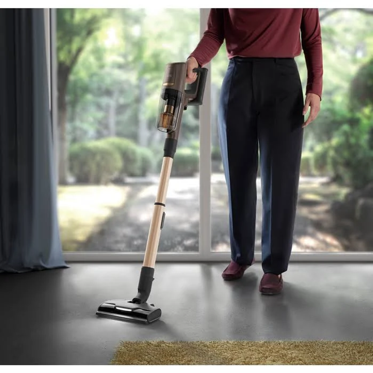 Eine Person hält einen Staubsauger. Der Staubsauger ist aufrecht und hat ein Gold- und Schwarz-Design.