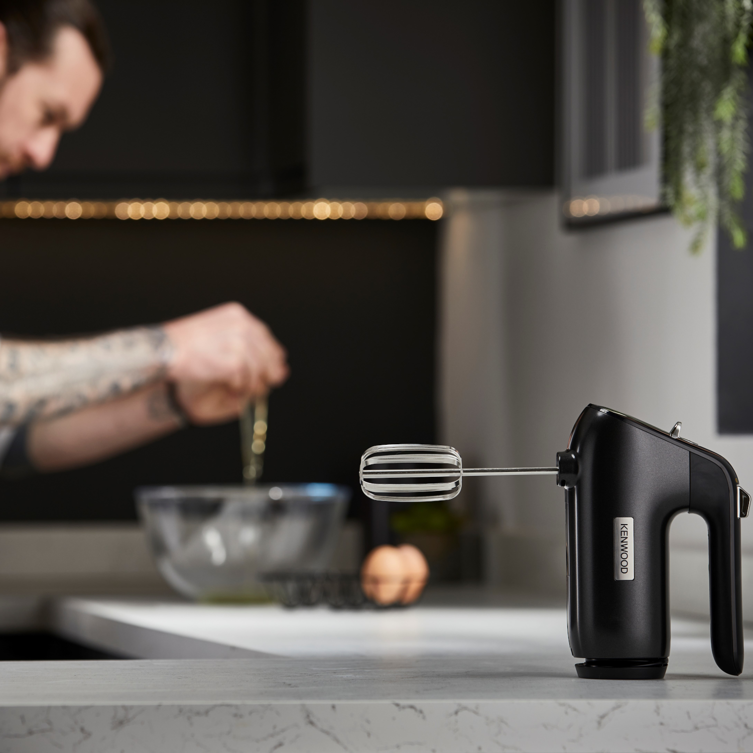 Ein Mann benutzt einen schwarzen Handmixer auf einer Küchenarbeitsplatte.