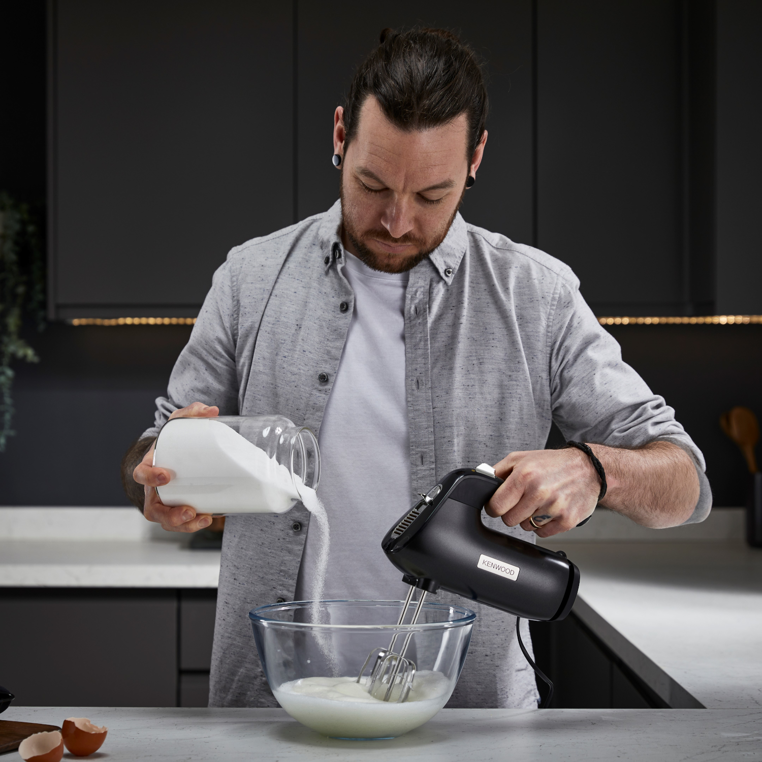 Mann, der Zucker in eine Schüssel mit einem Mixer gießt. Küchenumgebung.