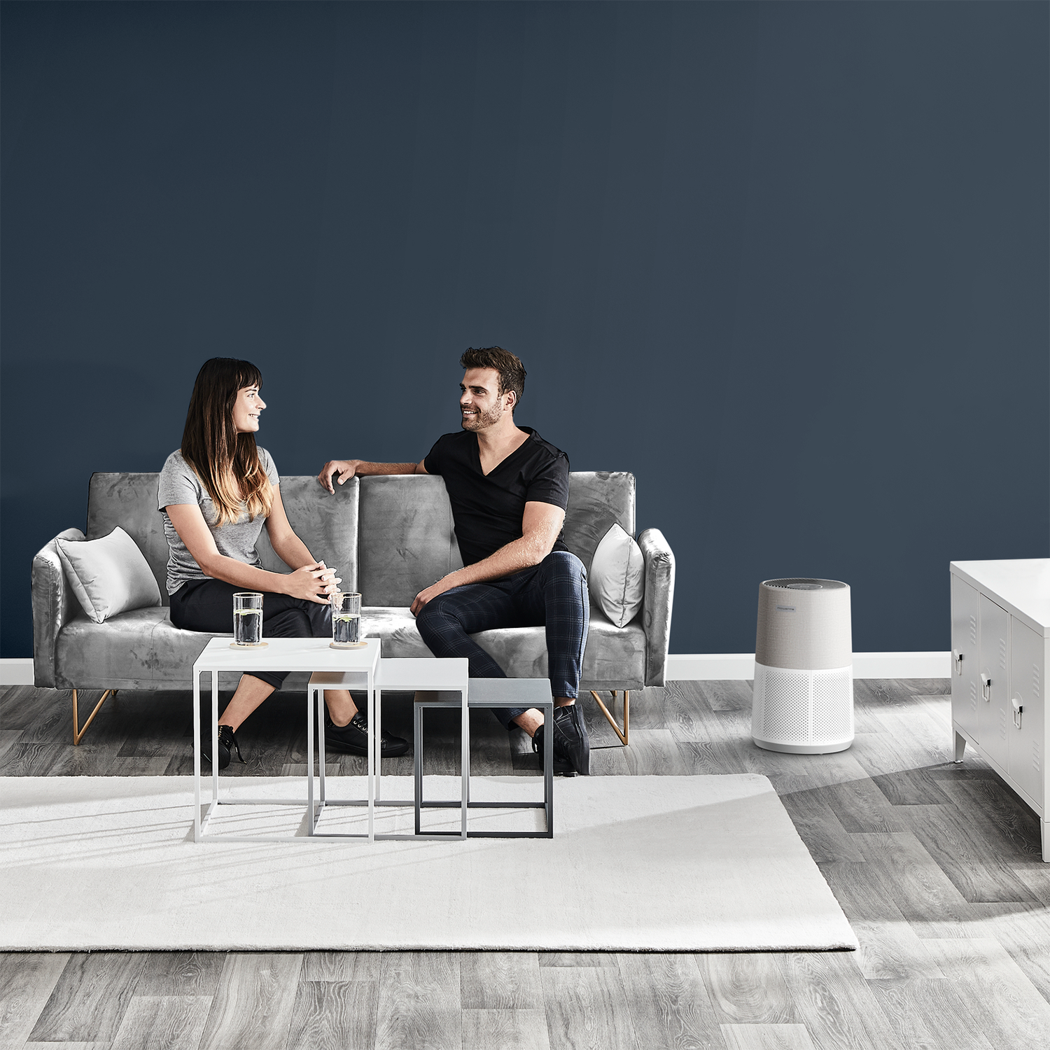 Paar auf einem Sofa in einem modernen Wohnzimmer. Luftreiniger vorhanden.