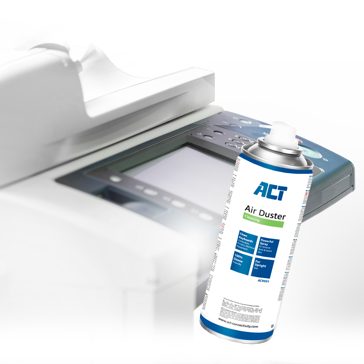 An air duster spray is held in front of an office machine. The spray can has labels and a white nozzle.