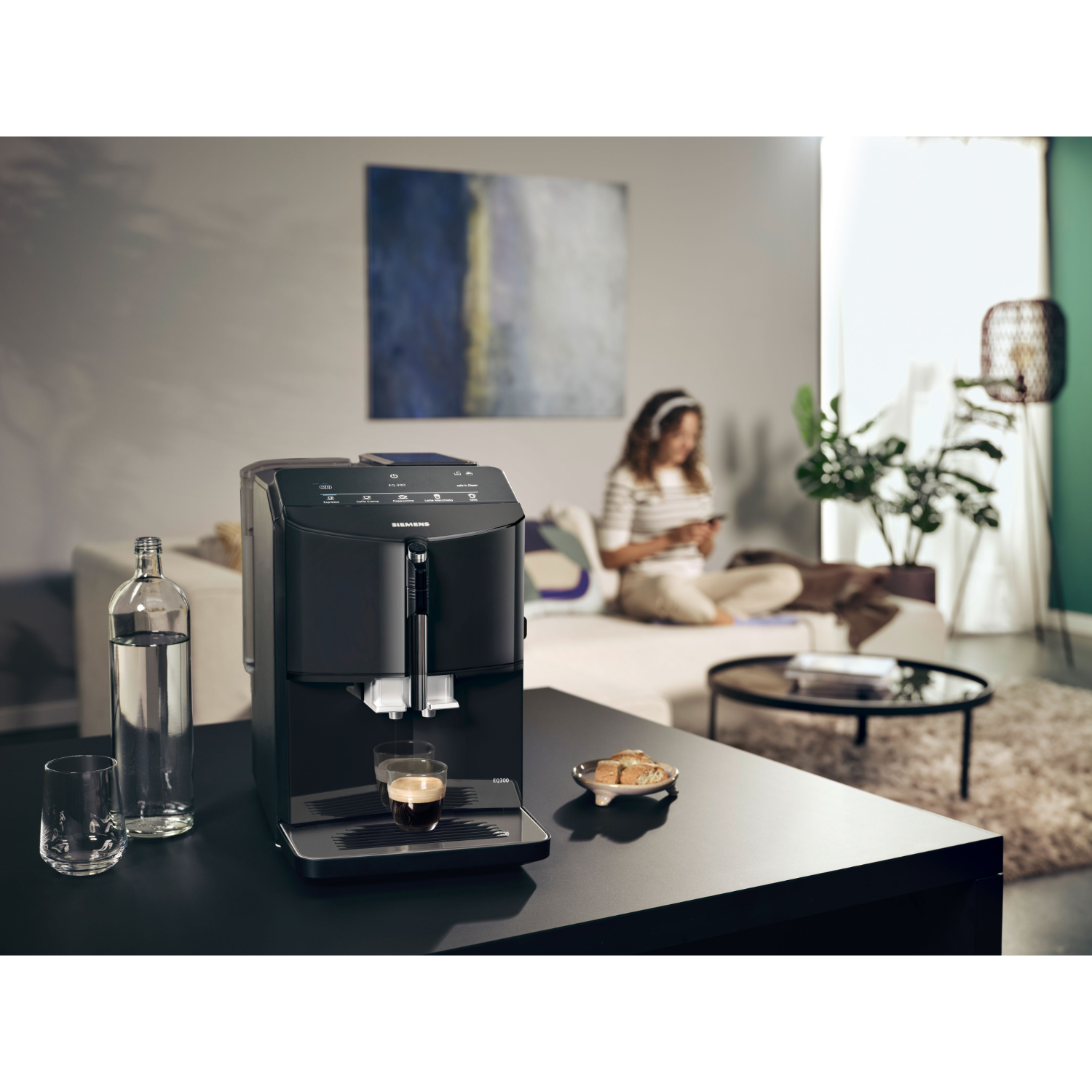 Czarny ekspres do kawy ze szklanką kawy na czarnym stole. Osoba w tle.