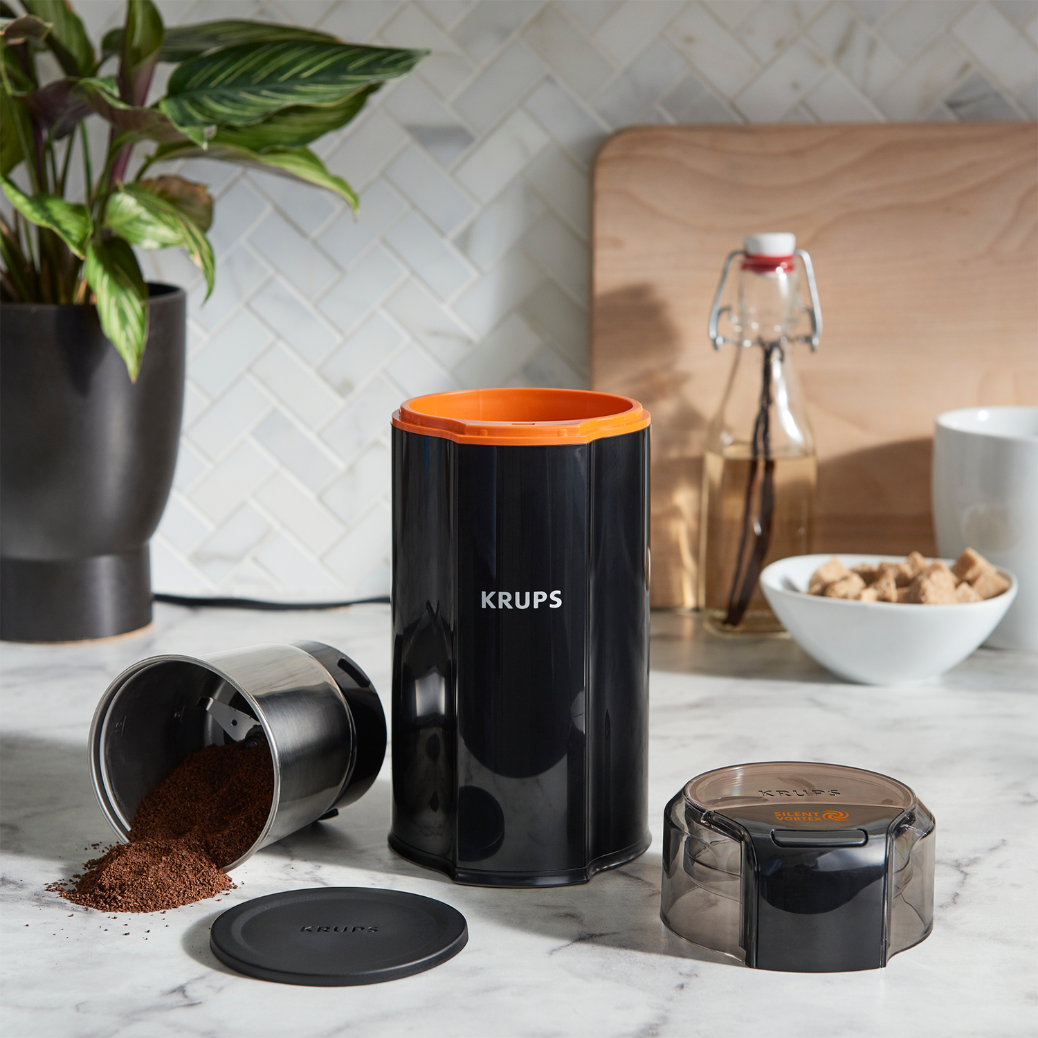 Młynek do kawy z rozsypaną kawą. Elementy na marmurowej powierzchni i pomarańczowy akcent.
