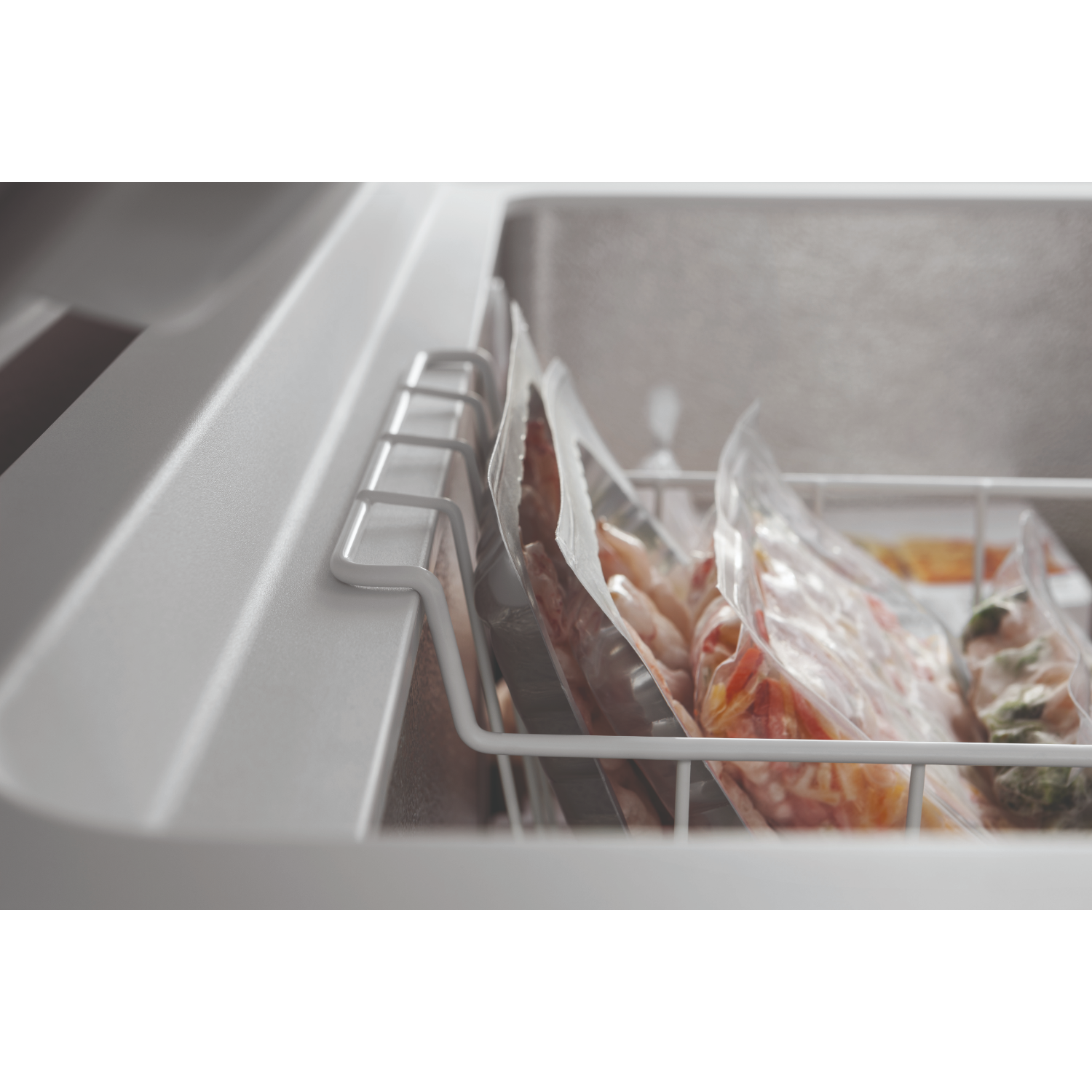 All'interno di un congelatore, diversi sacchetti sigillati di cibo in un cestello di filo bianco.