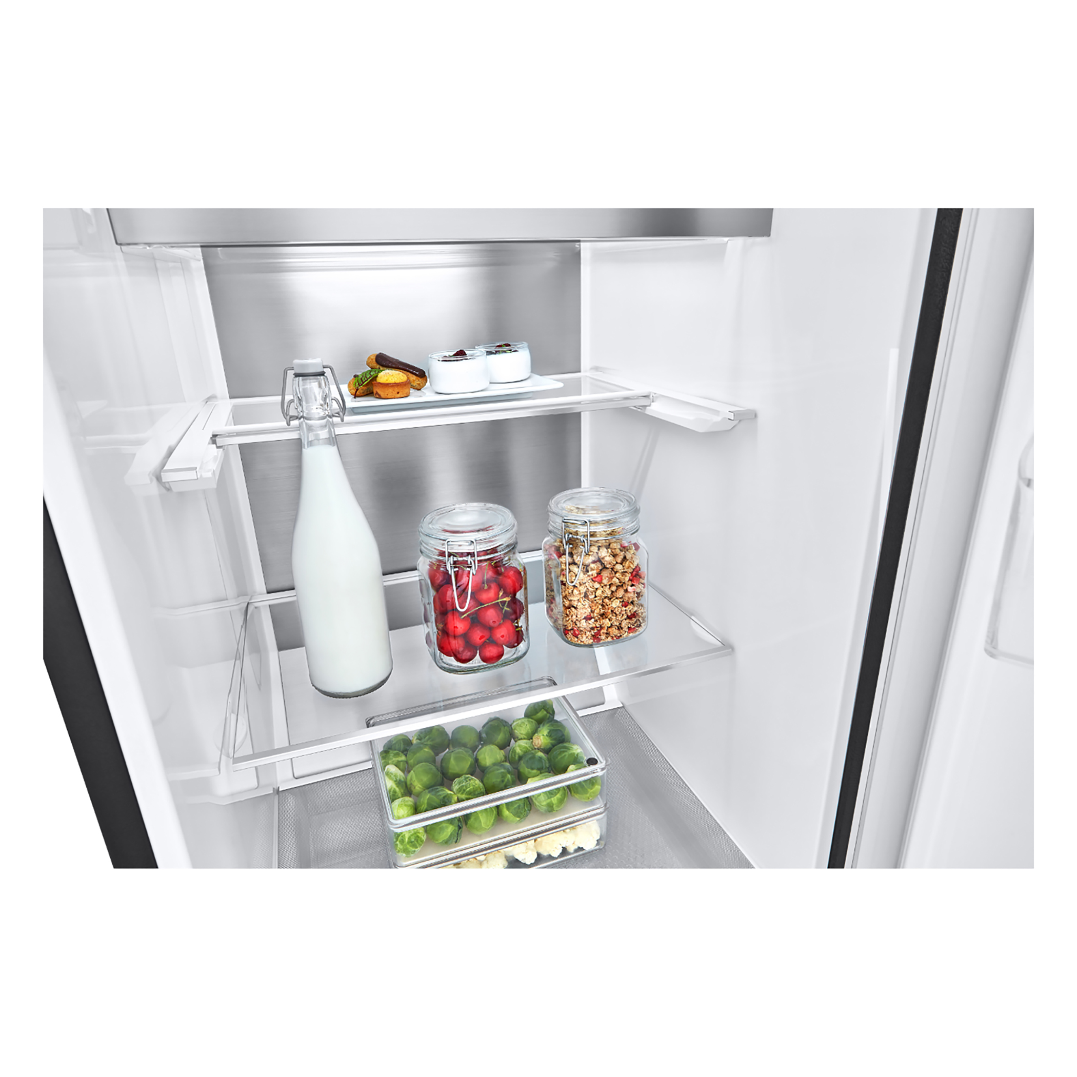 Interior de refrigerador. Estantes de vidrio con alimentos: leche, bayas y brotes. Parte trasera de acero inoxidable.