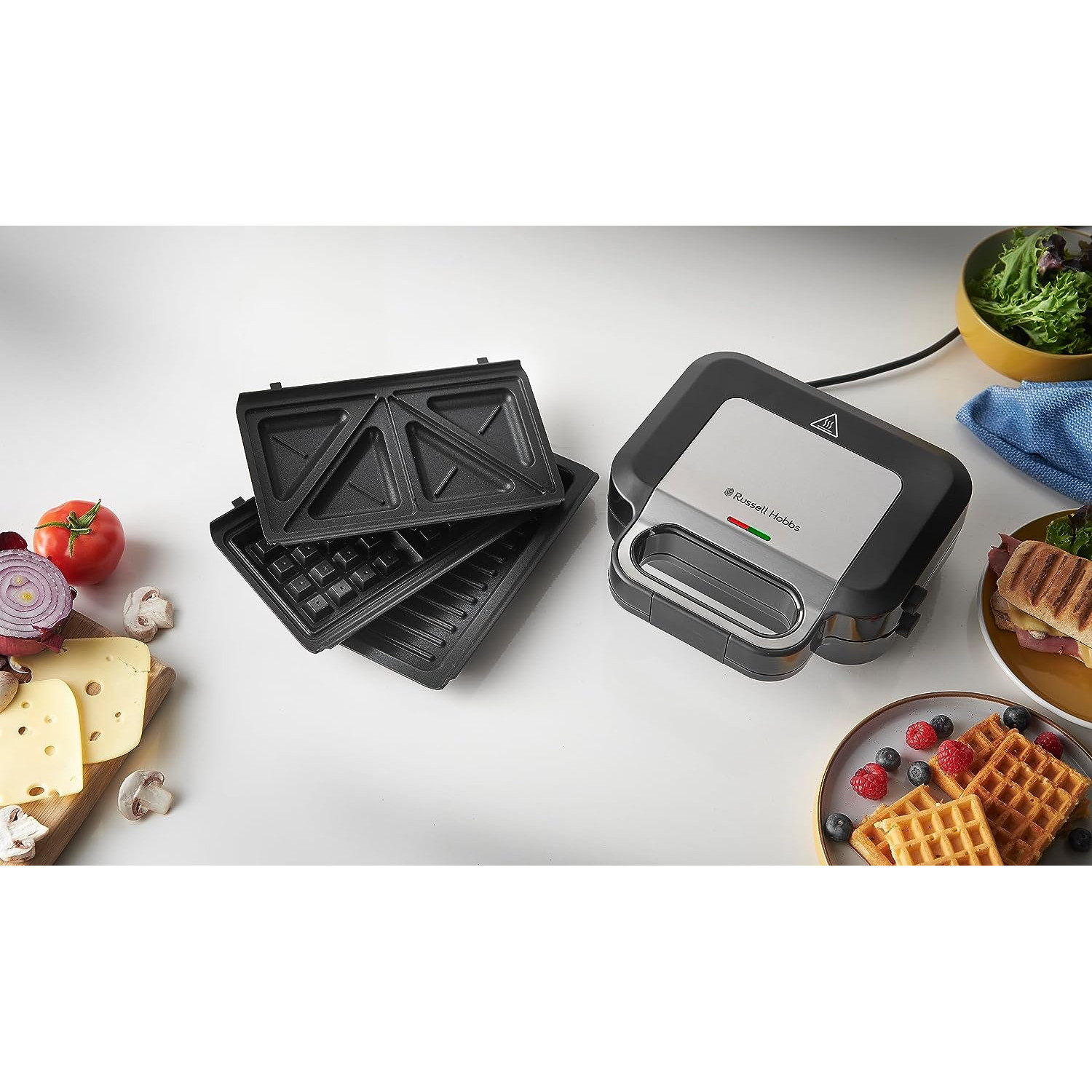 Ein schwarz-silberner Russell Hobbs Sandwichmaker mit offenen Platten und Waffeln mit Zutaten.