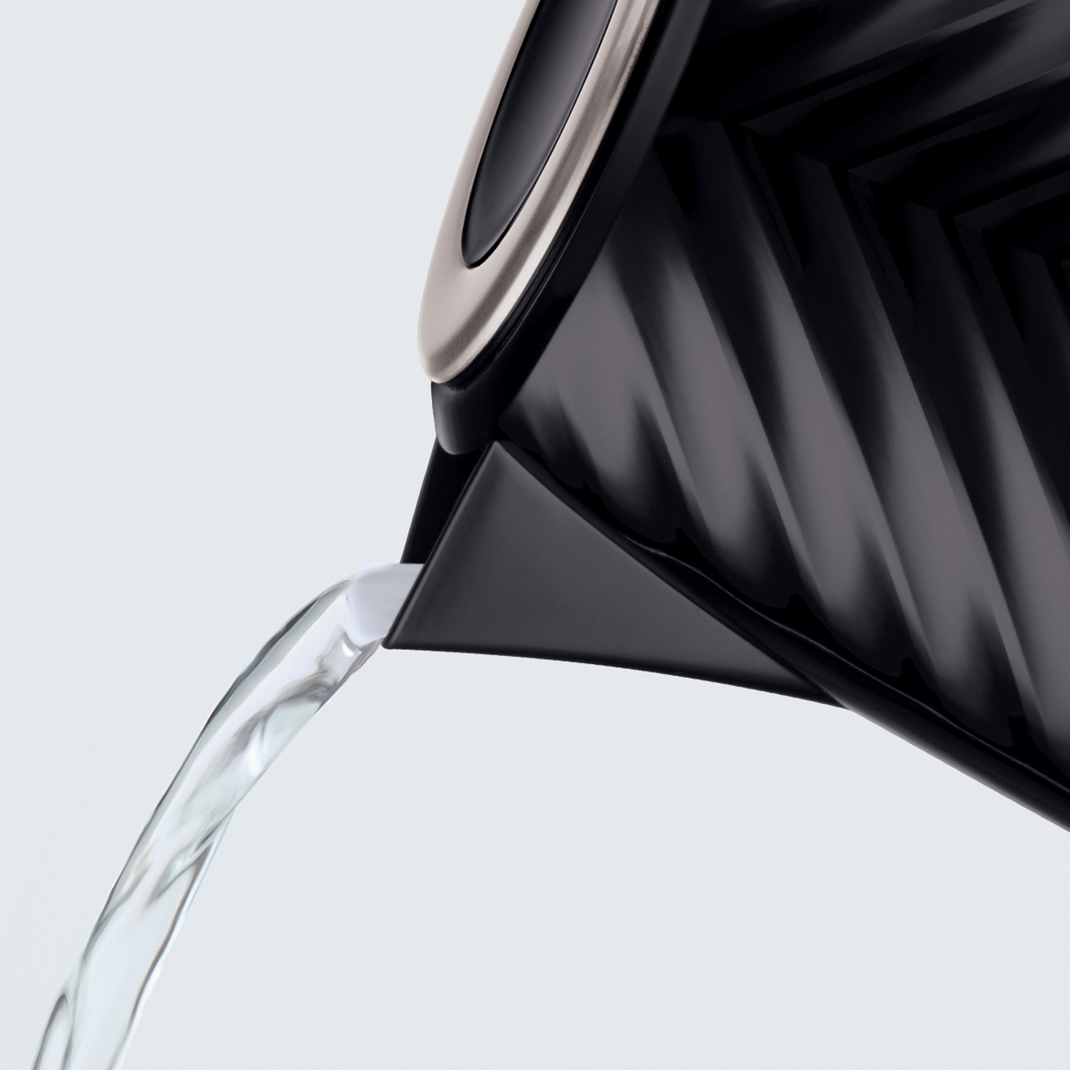 Woda wylewająca się z czarnego czajnika elektrycznego ze srebrnym wykończeniem. Białe tło.