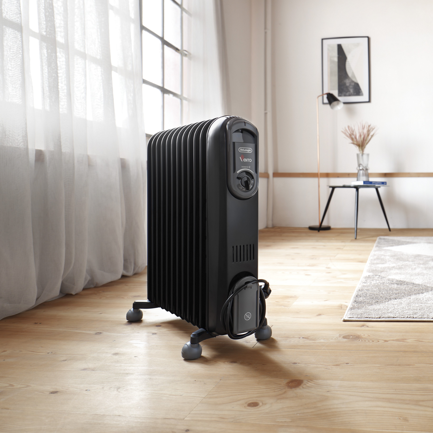 Zwarte oliegevulde radiator op wielen. In een woonkamer met een raam.