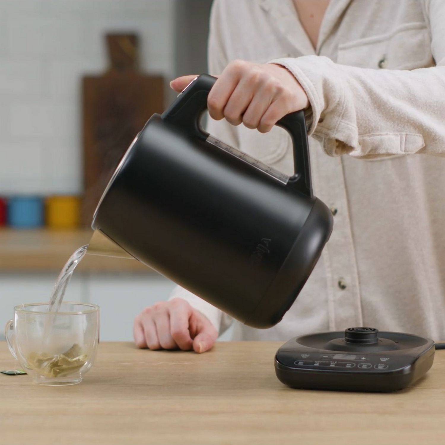 Kobieta nalewa wodę z czarnego czajnika Ninja do szklanki.