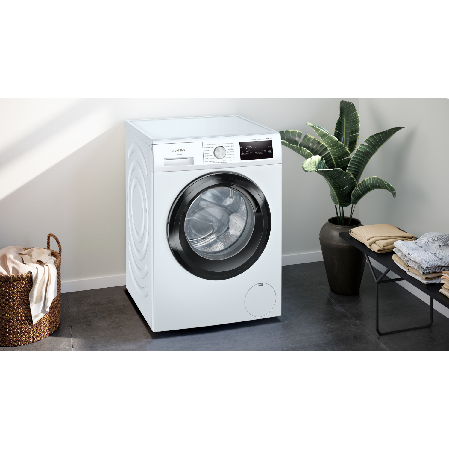 White washing machine in a room. Black door, plant in the background. Laundry basket.