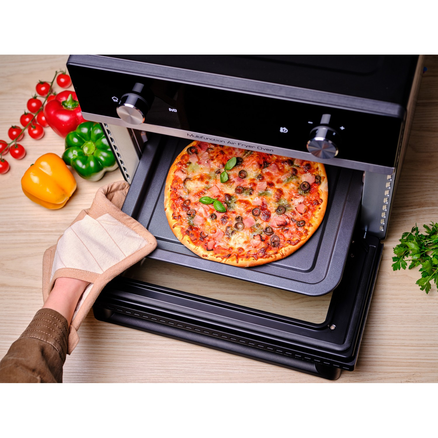 Piekarnik z frytkownicą powietrzną z pizzą na tacy i osobą trzymającą rękawicę kuchenną.