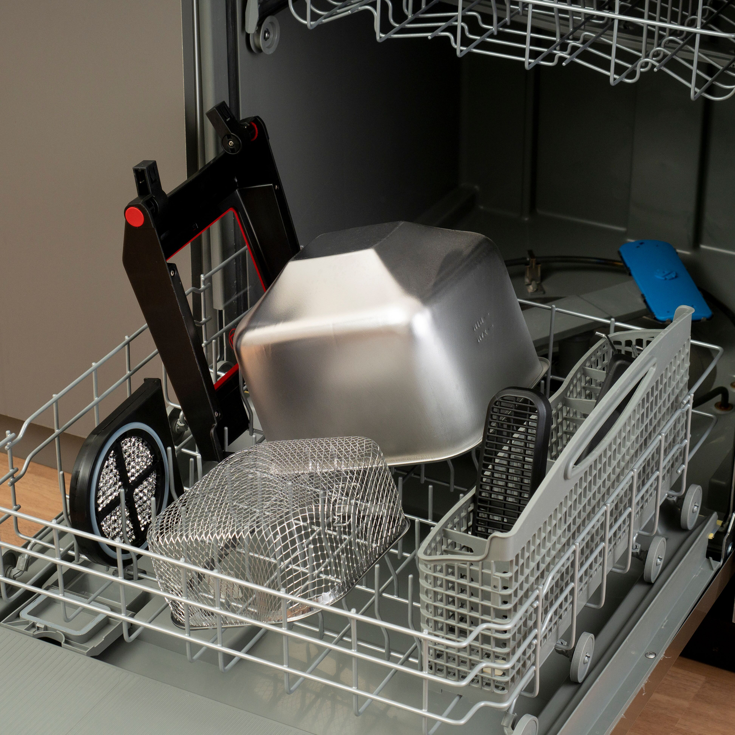 Wnętrze zmywarki z różnymi przedmiotami, w tym metalową miską.