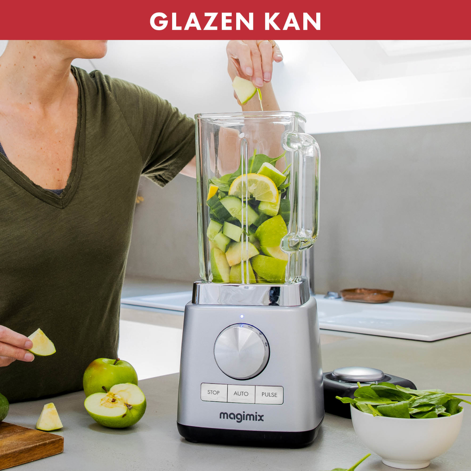 Persoon voegt appelschijfjes toe aan een blender. Blender is zilver, heeft een glazen container. Keukenomgeving met groene appels.