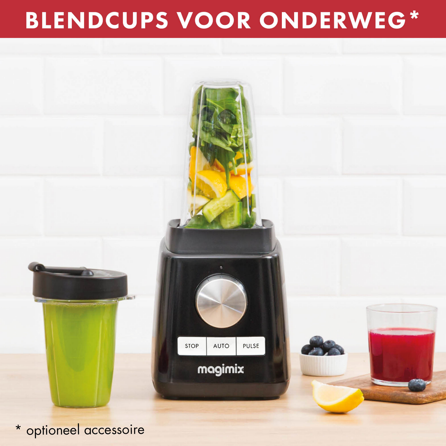 Zwarte blender met bevestigde beker. Groene smoothie in beker, sap en bosbessen opzij. Witte betegelde achtergrond.