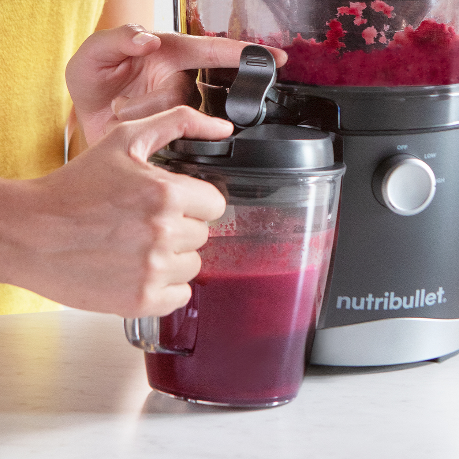 Woman's hands using a Nutribullet. Blended purple liquid in a cup, and the machine.