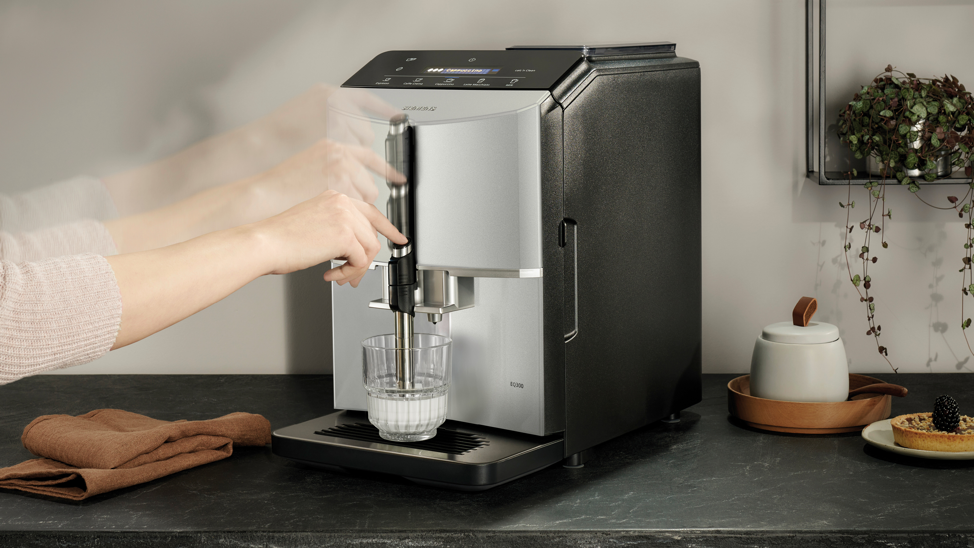Una persona che aziona una macchina per caffè espresso argento e nera, versando latte in un bicchiere.