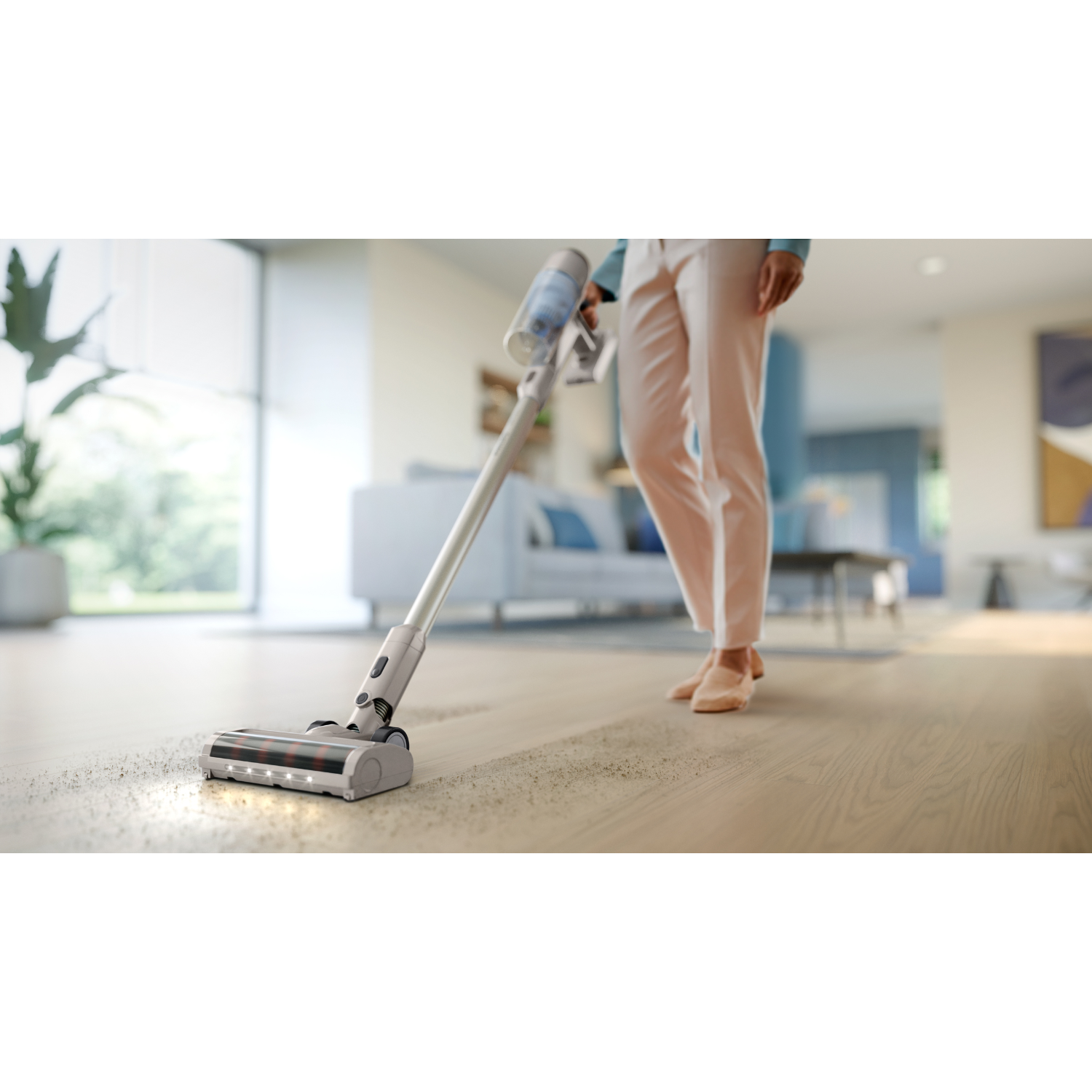 Osoba odkurzająca drewnianą podłogę odkurzaczem bezprzewodowym. Jasny pokój z białymi ścianami.