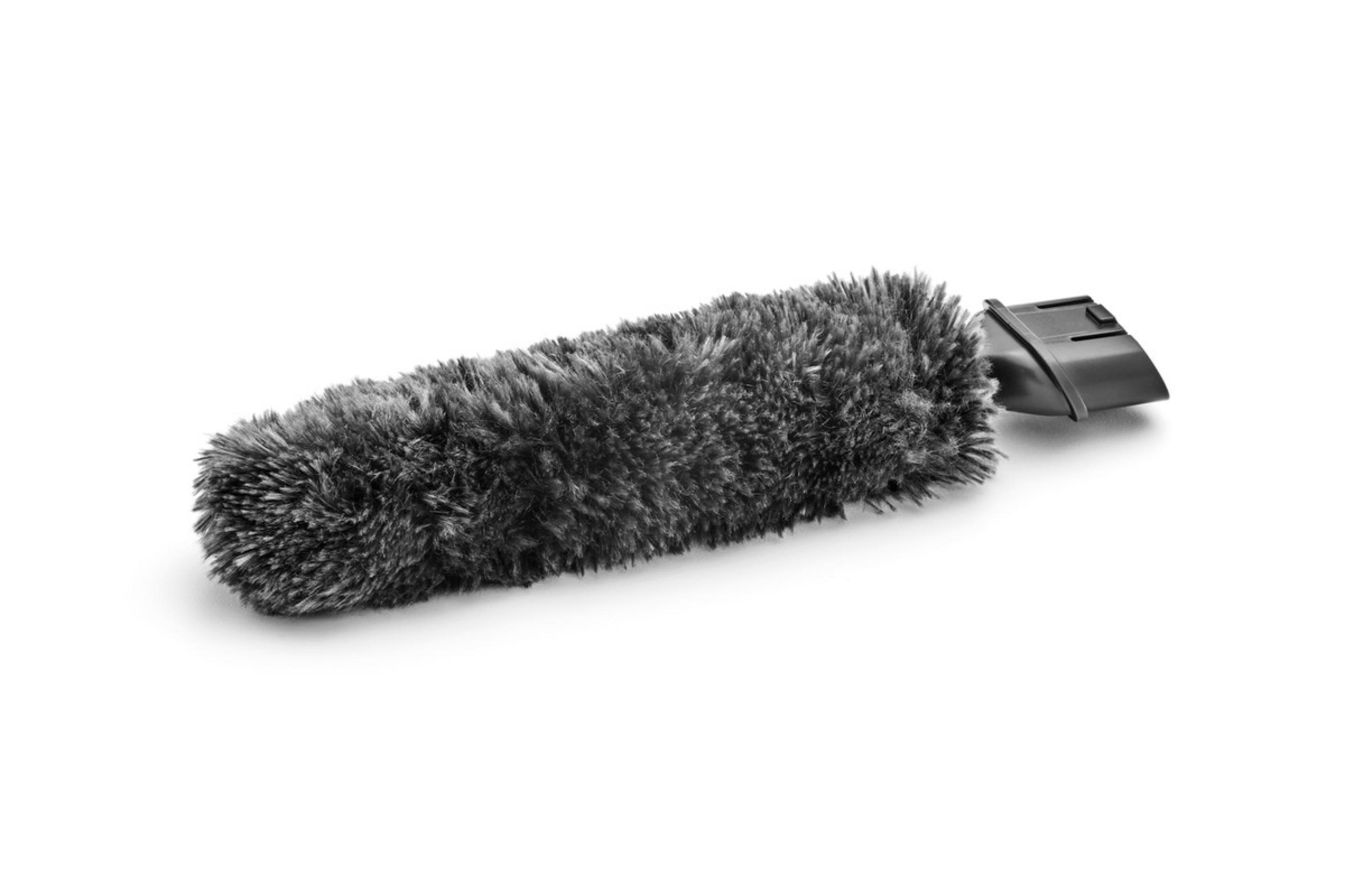 Puszyste, szare narzędzie do czyszczenia, leżące na białej powierzchni. Ma czarny uchwyt.