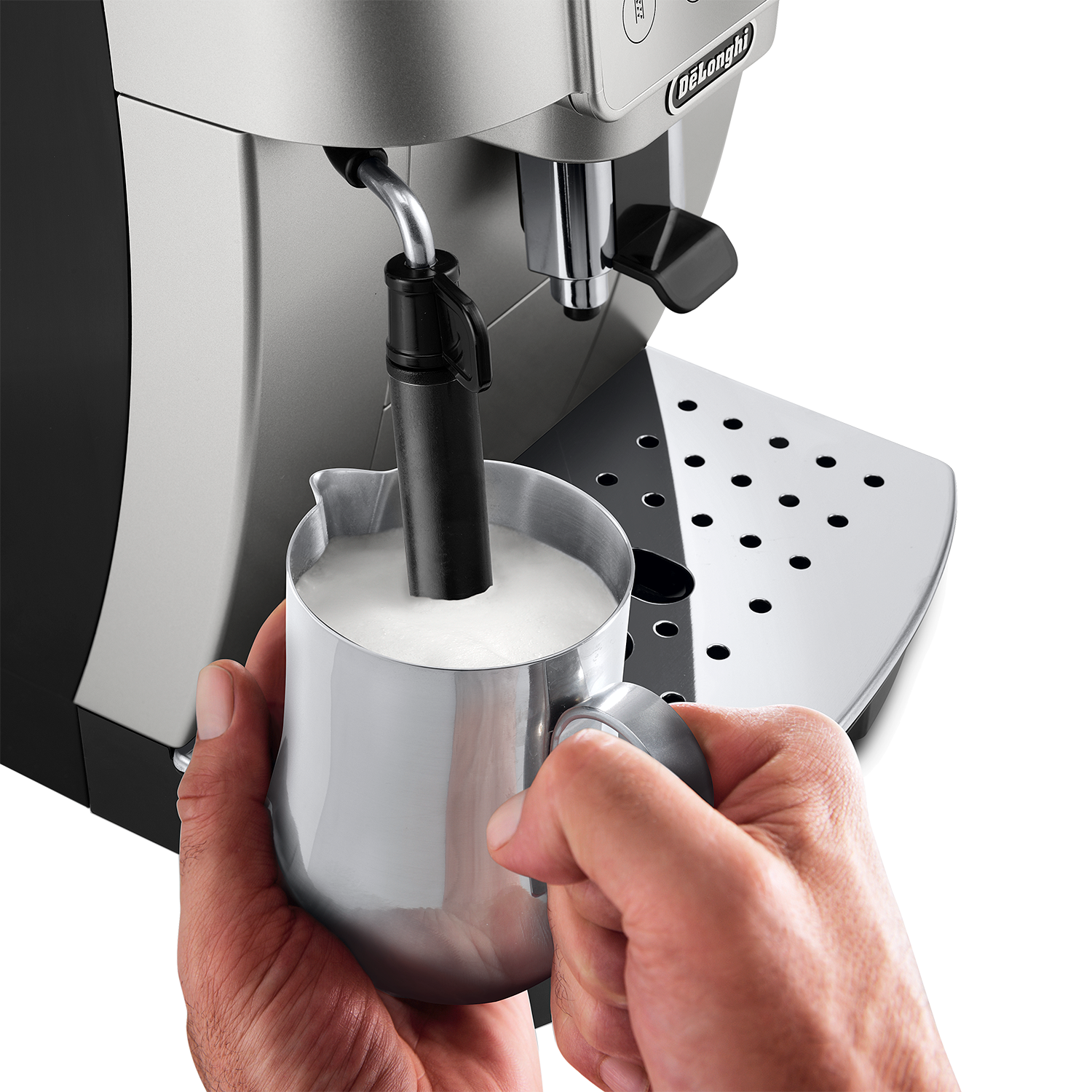 Hands holding a metal milk pitcher, frothing milk with coffee machine.