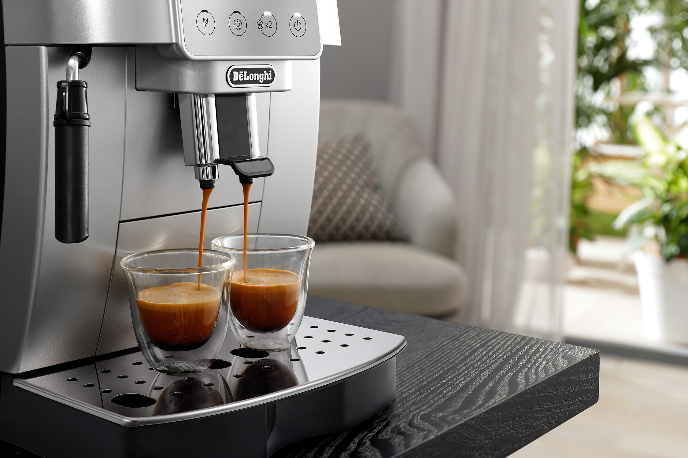 Espresso machine dispensing coffee into glass cups. Background includes a table and a blurry interior.