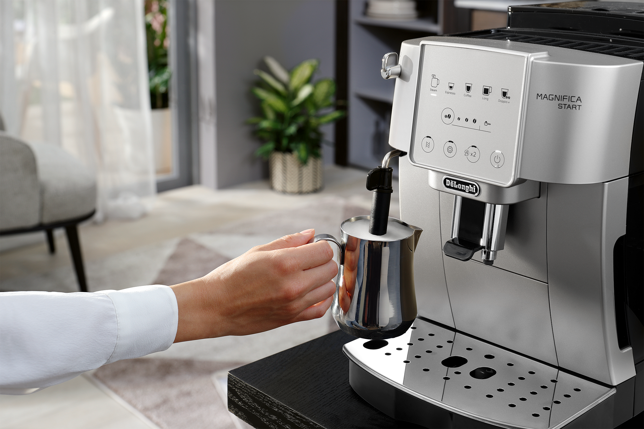 Coffee machine, DeLonghi, with milk frothing. Woman's hand and home setting.