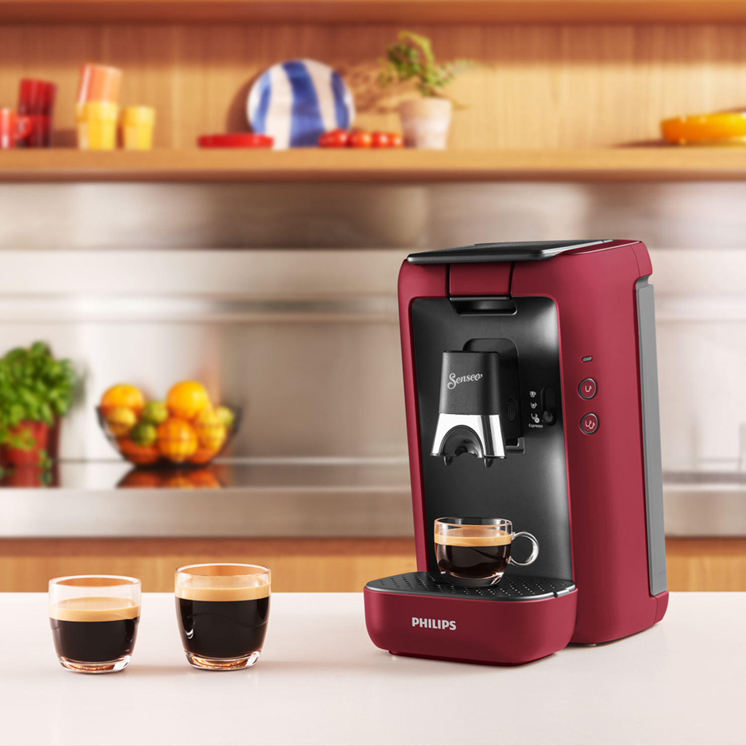 Ein roter Kaffeezubereiter mit einer Tasse Kaffee und zwei Gläsern Kaffee auf einer weißen Oberfläche.