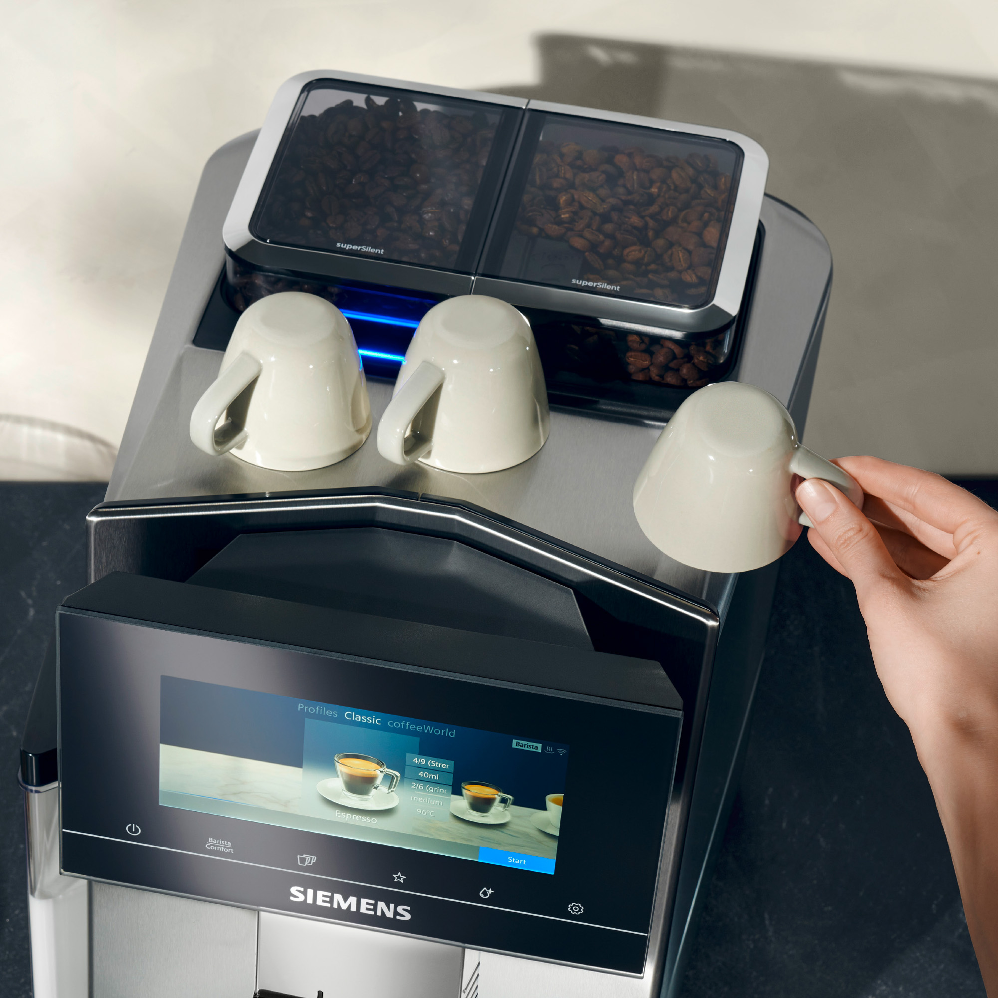 A coffee machine with cups and coffee beans containers. A hand is holding a cup.