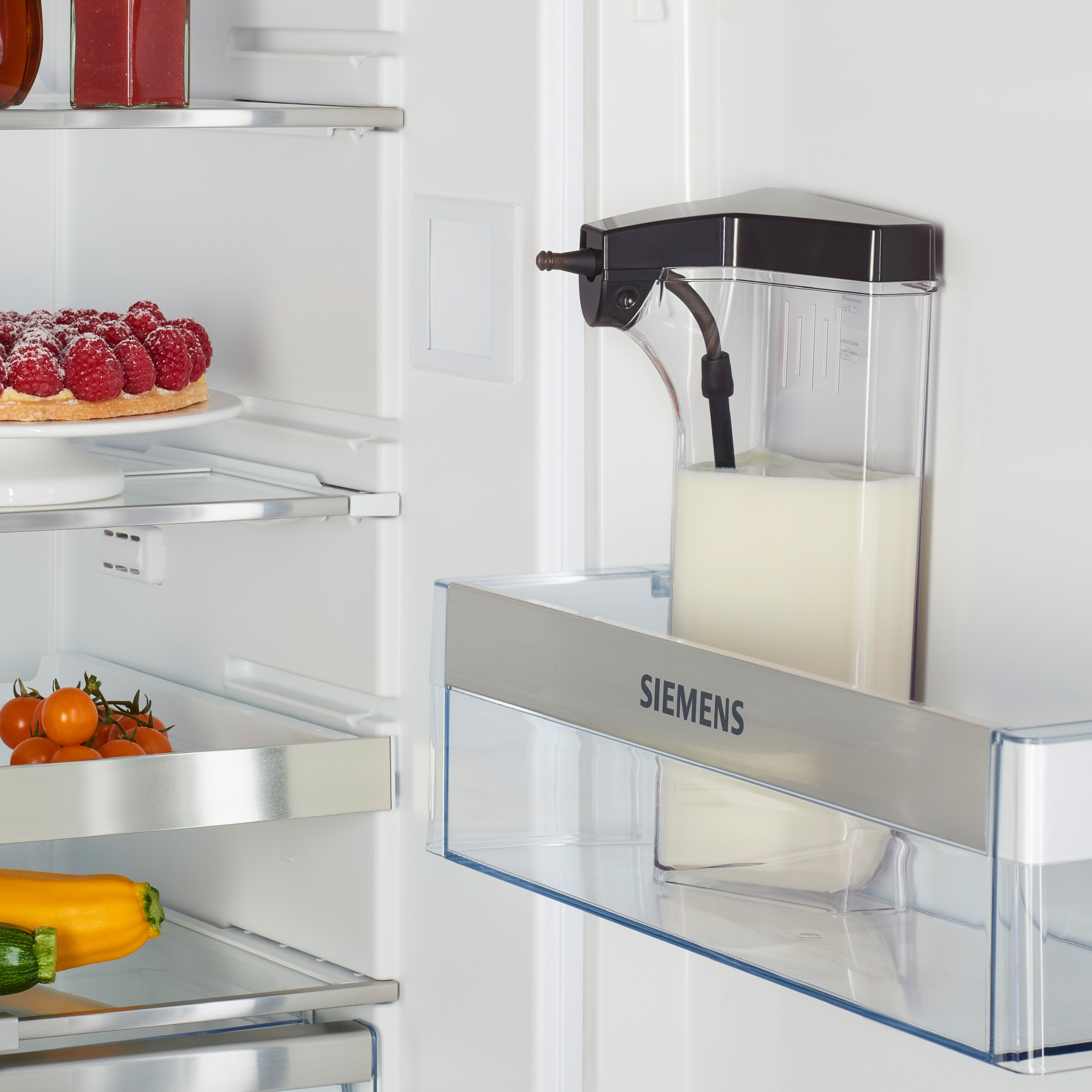 Inside of a fridge. A glass container with milk and a plate of food.