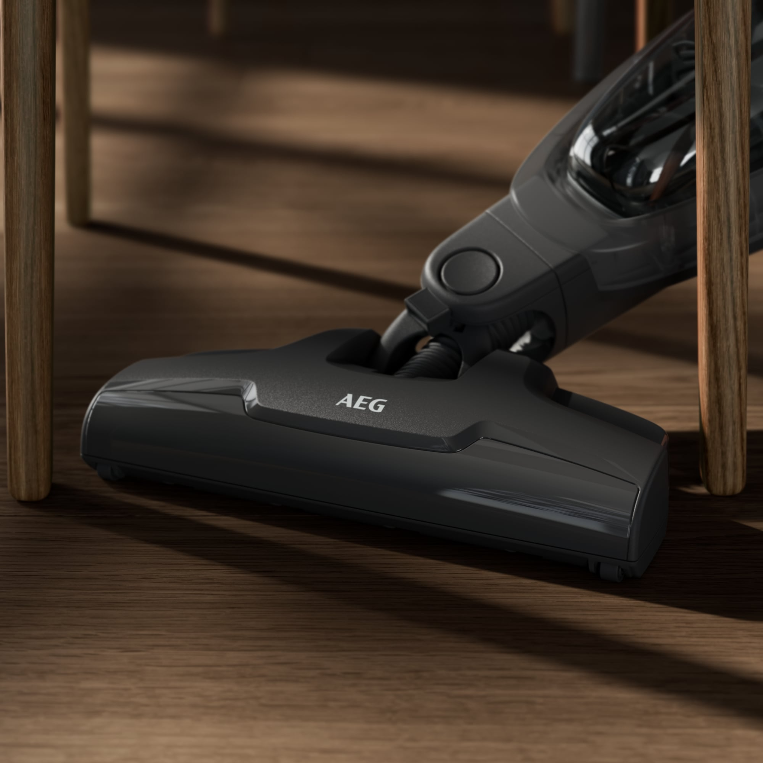 Dark gray AEG vacuum cleaner head, between wooden chair legs.