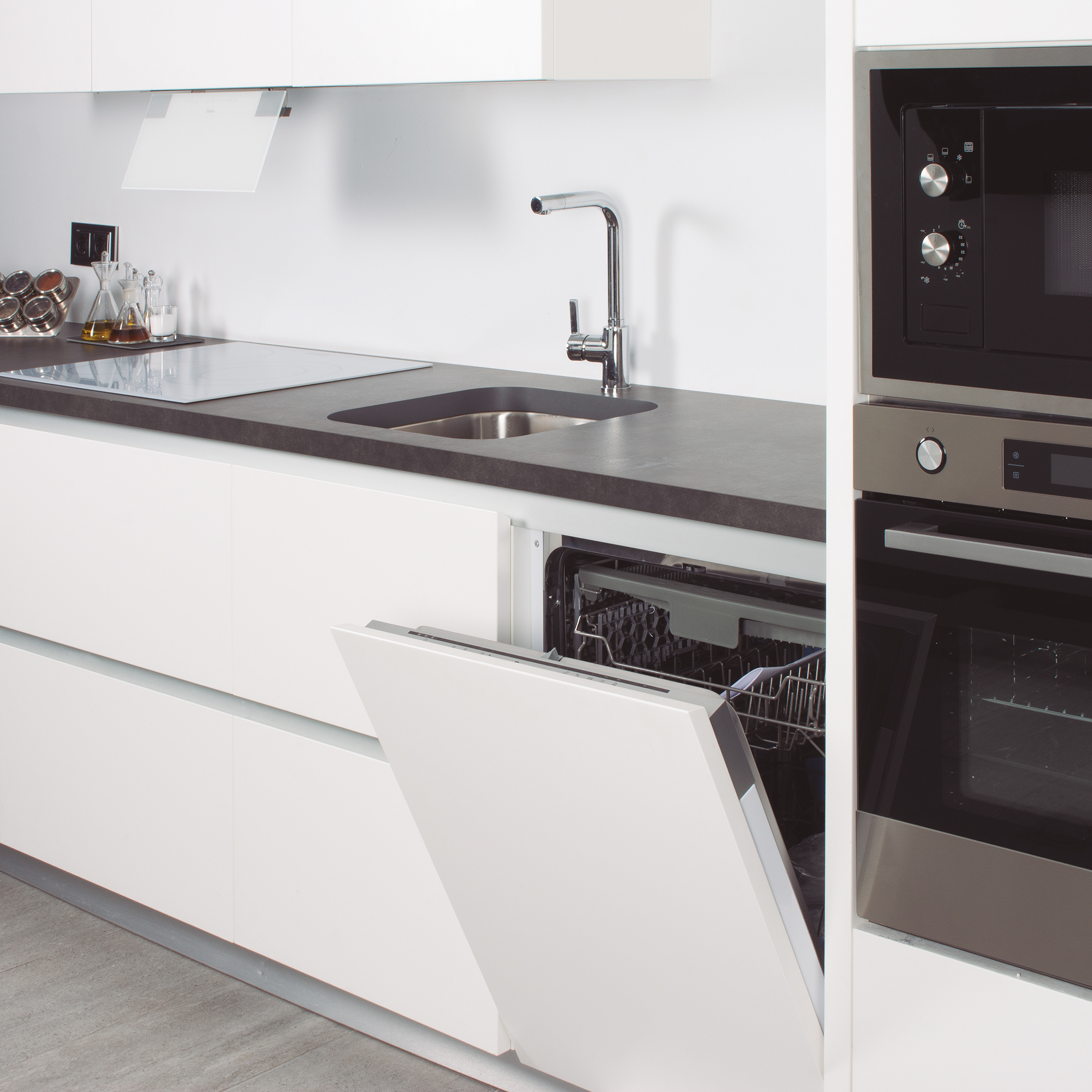 Cocina moderna con armarios blancos y encimera negra. Una puerta de lavavajillas está abierta. Microondas arriba.