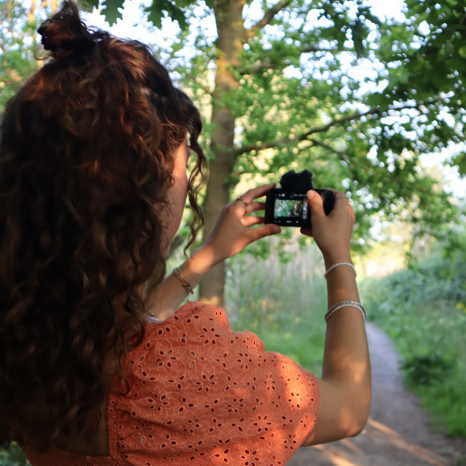 Mujer tomando una foto con una cámara. Al aire libre, con un fondo verde y borroso.