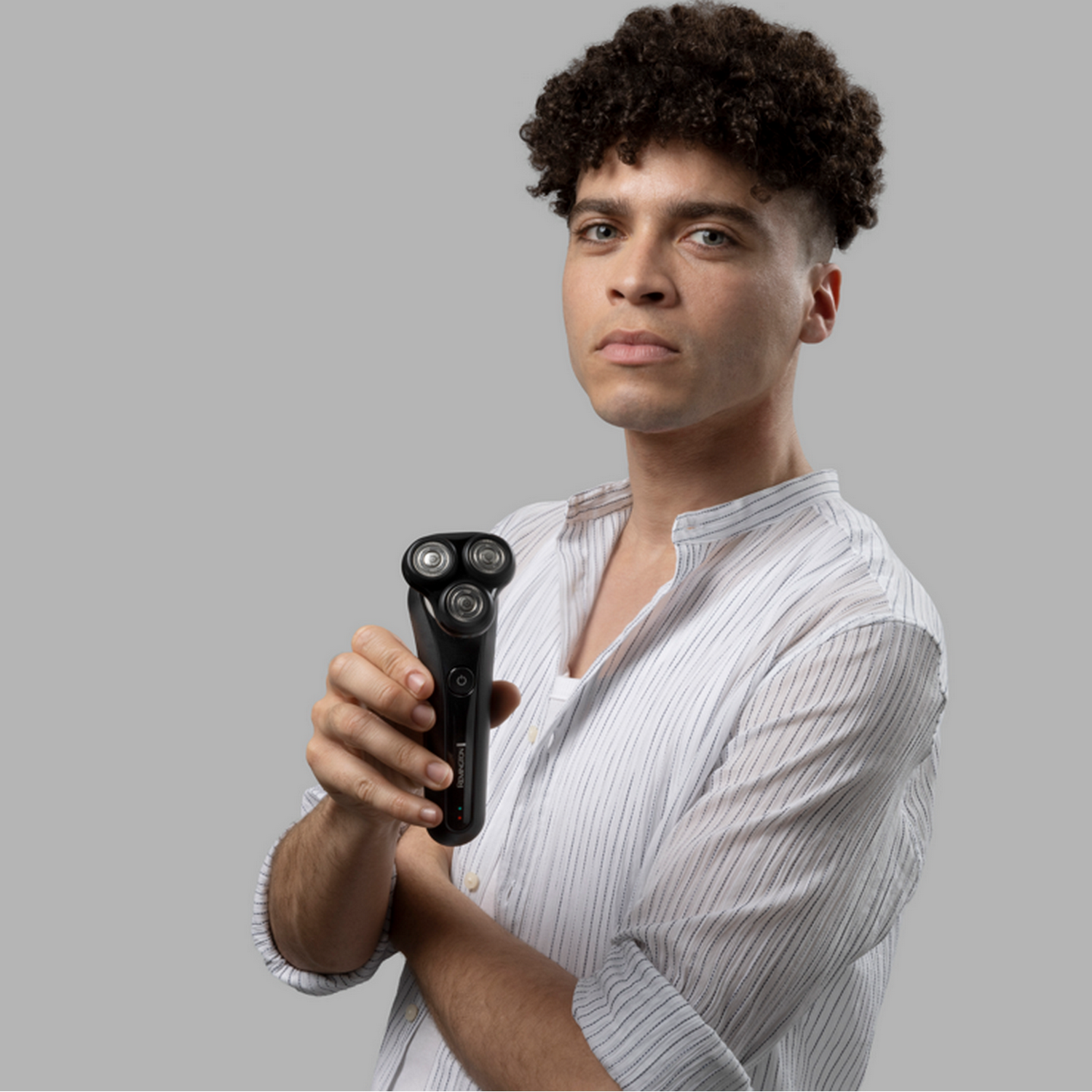 Un uomo con i capelli corti e ricci, che tiene un rasoio rotante Remington nero, guarda la fotocamera.