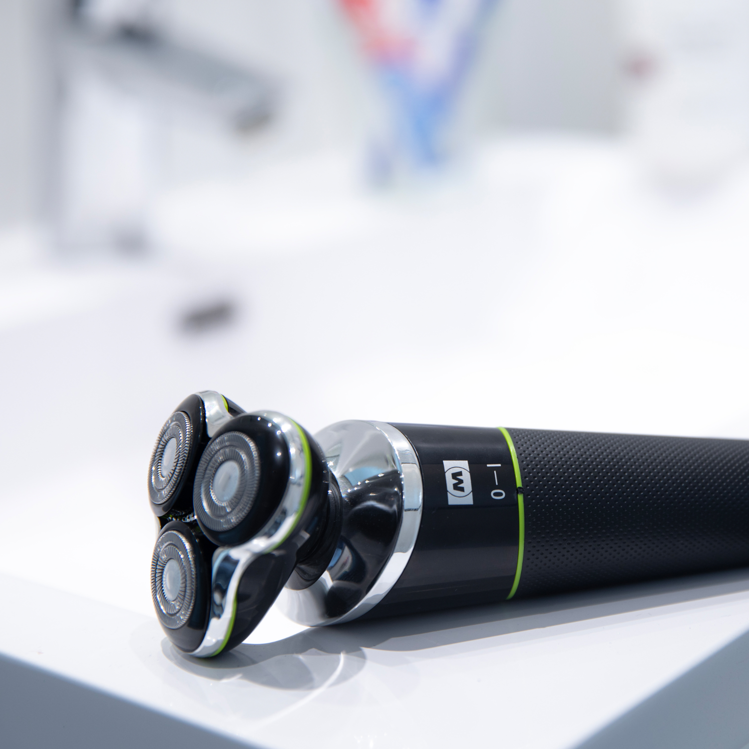 Golarka elektryczna na białej powierzchni z trzema obracającymi się głowicami, czarnym uchwytem i zielonymi akcentami.