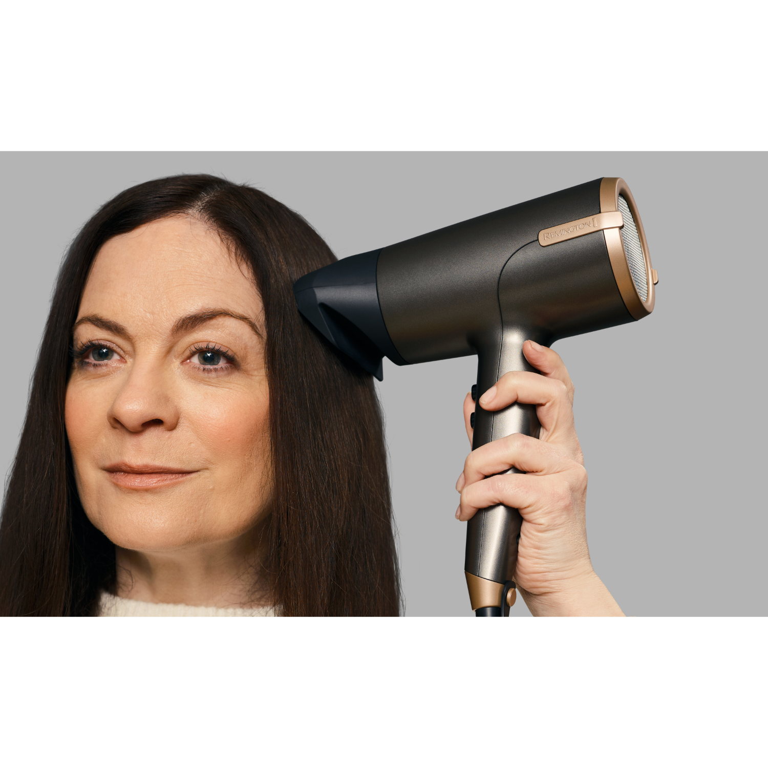Eine Frau benutzt einen Haartrockner, der Haartrockner ist grau und gold.