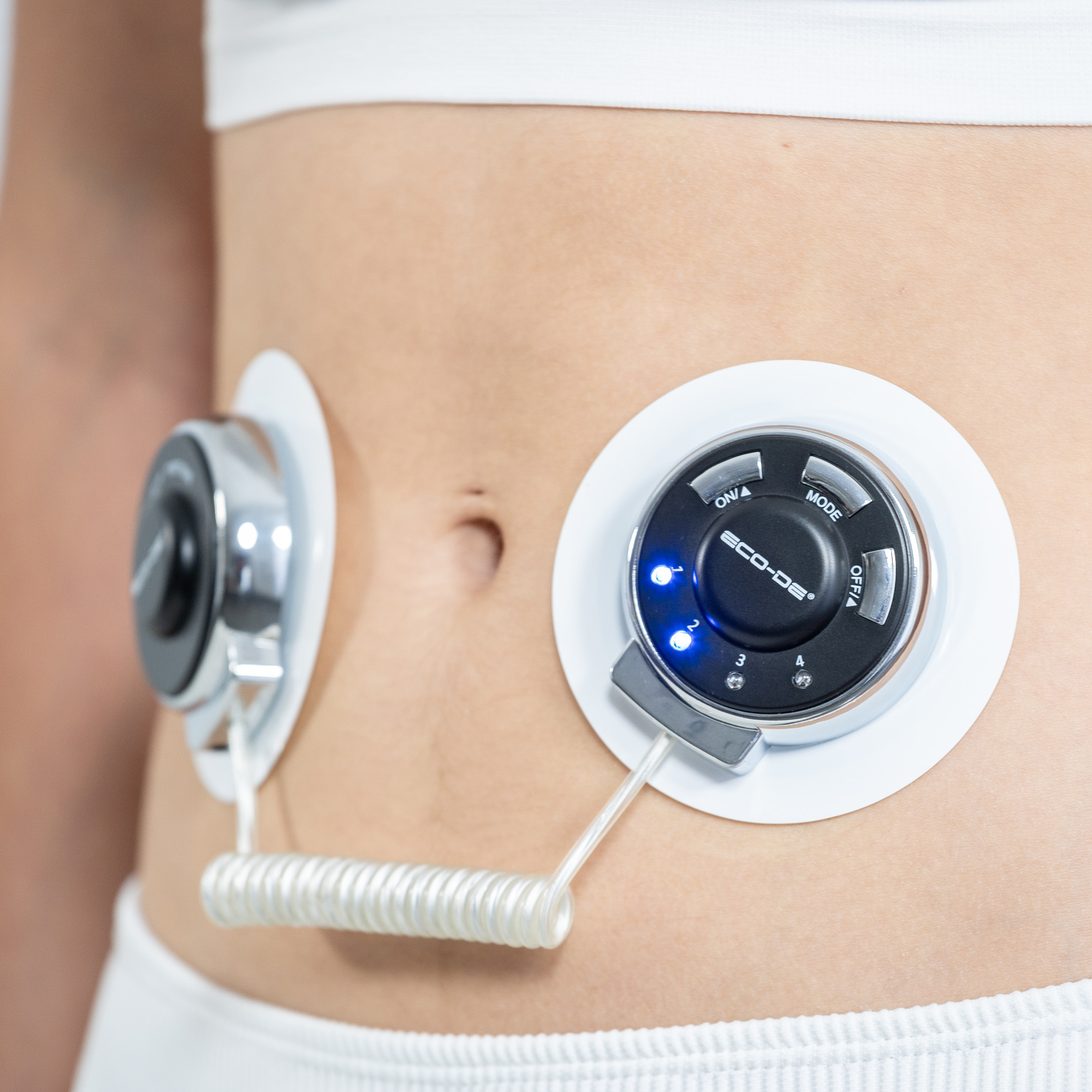 Abdomen de una persona con dos dispositivos médicos adjuntos, almohadillas blancas y luces azules.