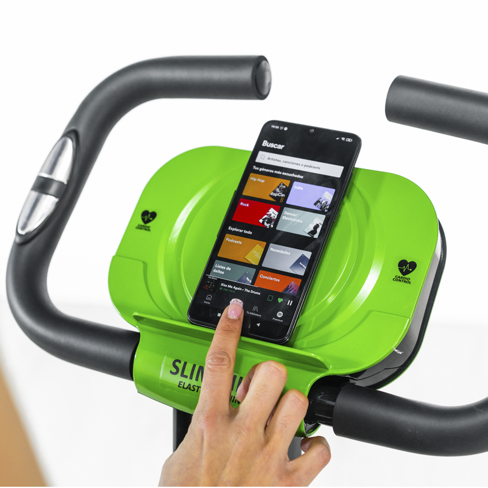 Persona toca smartphone en consola verde de bici estática, mostrando app de música.