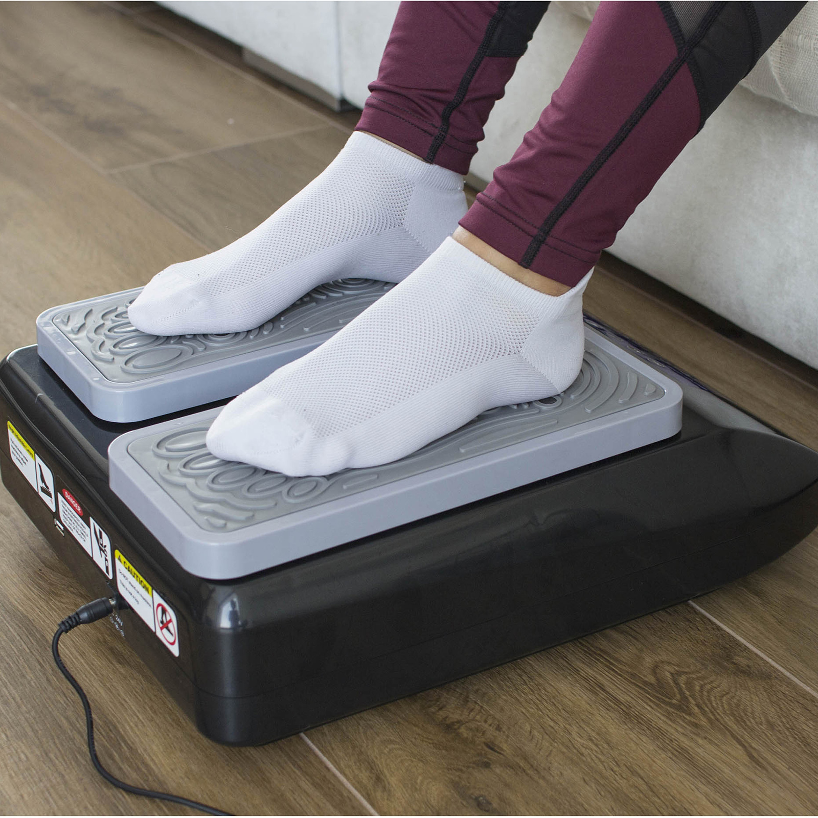 Pies de una persona con calcetines blancos en una plataforma vibratoria. Piernas con leggings granate.