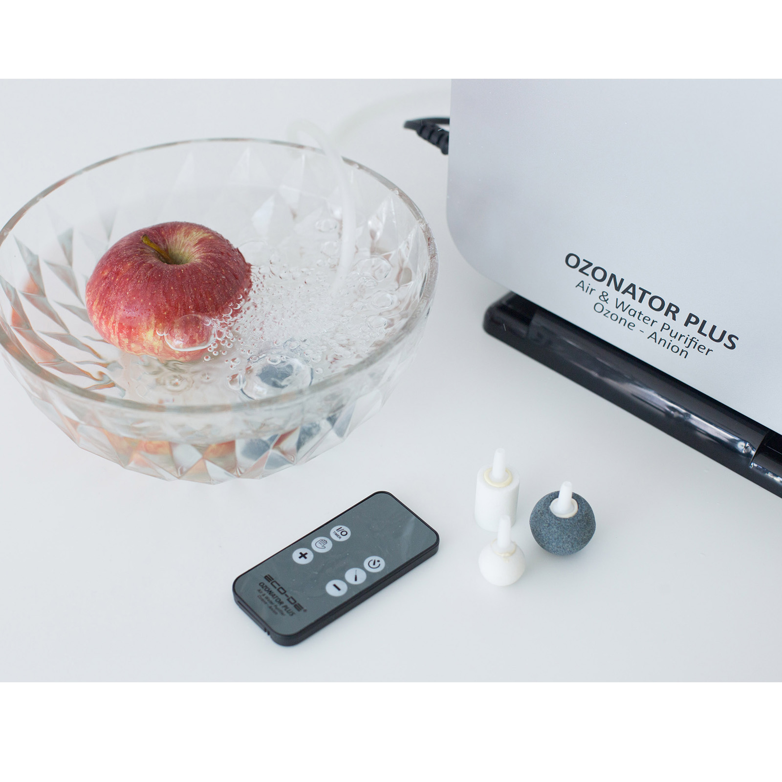 Una manzana roja en un cuenco de cristal con agua. Una máquina de ozono blanca en el fondo con accesorios.