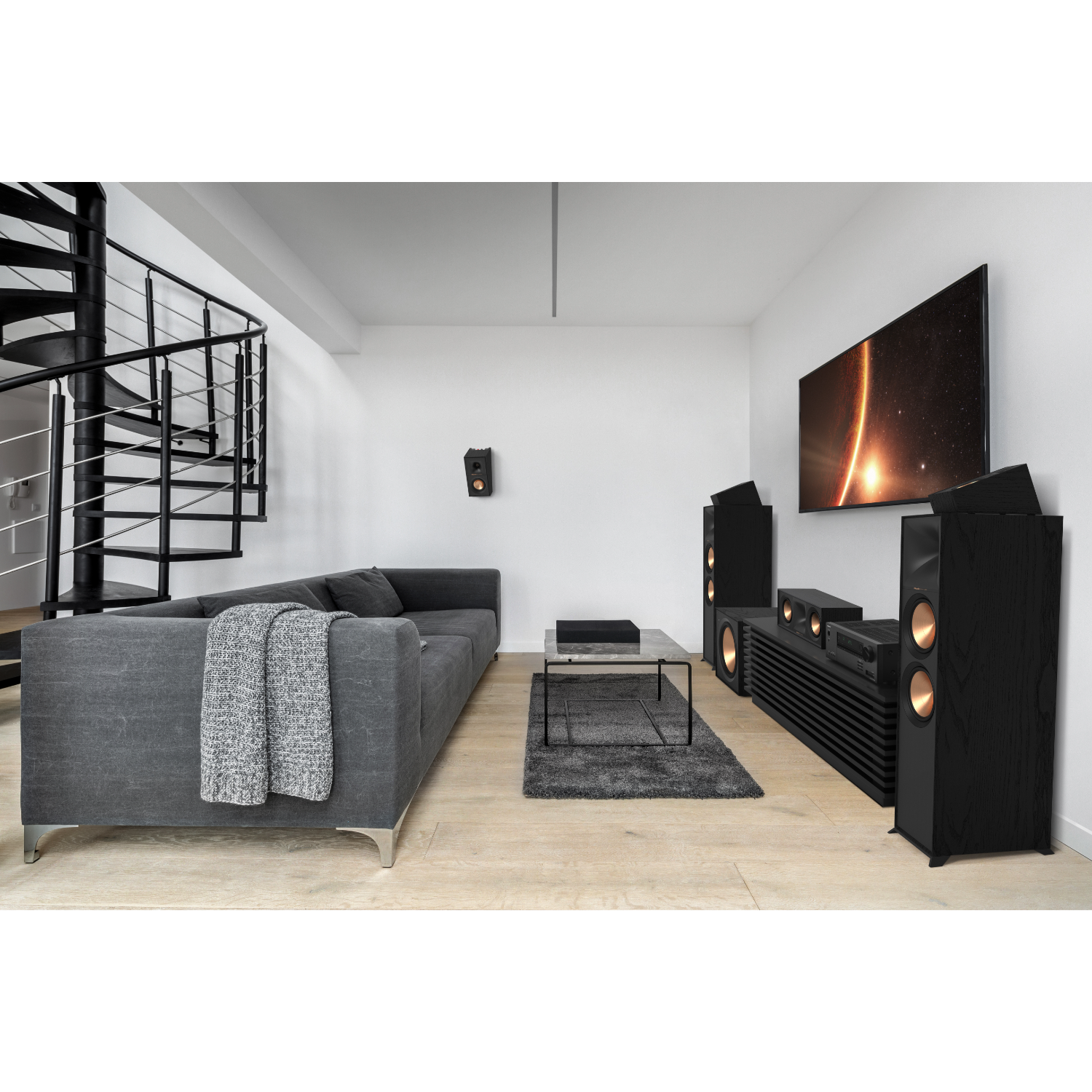 Salon z szarą sofą, głośnikami, telewizorem i kręconymi schodami.