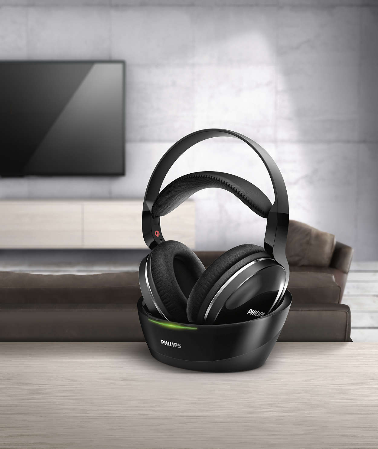 Auriculares Philips negros en base de carga, mesa de madera, fondo borroso.