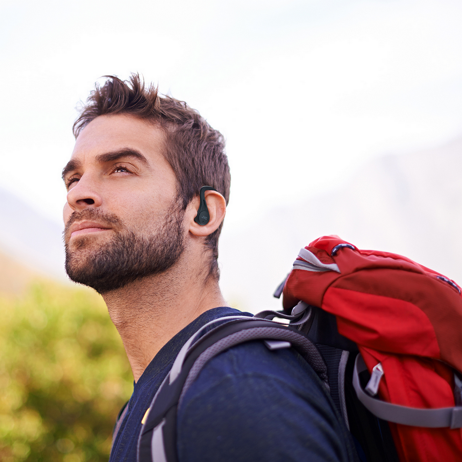 Mężczyzna wędrujący w naturze z plecakiem i słuchawką, patrzący w górę.