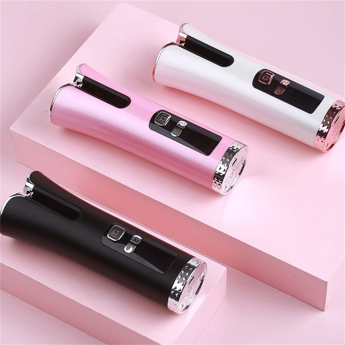Drei automatische Lockenwickler in Pink, Weiß und Schwarz. Sie befinden sich auf einer rosa Oberfläche.