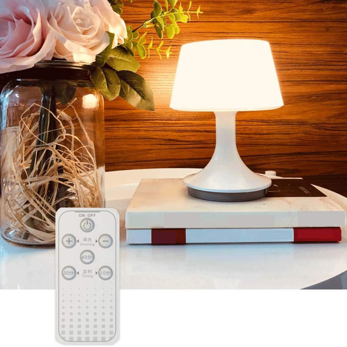 Weiße Lampe auf Büchern, Vase mit Blumen, Fernbedienung. Weißer Tisch, warmes Licht.